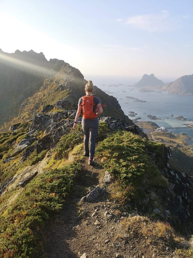 Astrid has her back turned against the camera as she stands on a steep mountaintop. 